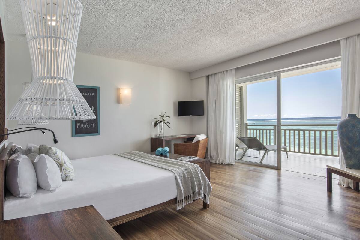 Une chambre d’hôtel moderne dotée d’un grand lit, d’un bureau, d’une télévision et d’un balcon offrant une vue sur l’océan.