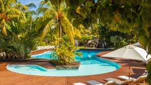 Une piscine entourée d’une terrasse en bois, de chaises longues et de palmiers.
