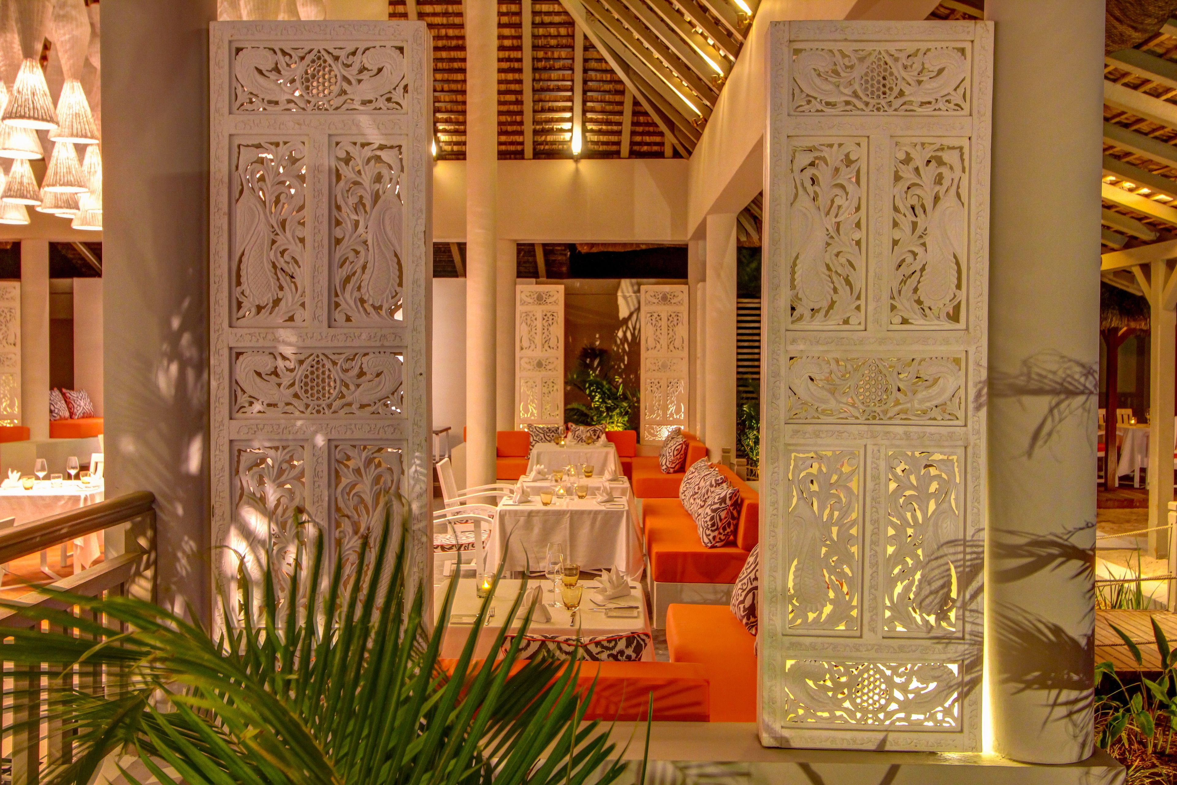 An indoor dining area with white ornate partitions, orange seating, and tables set for dining.
