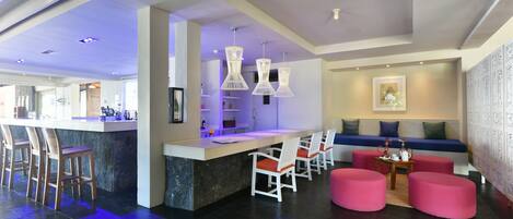 A modern hotel lobby with a bar area, seating, and a reception desk.