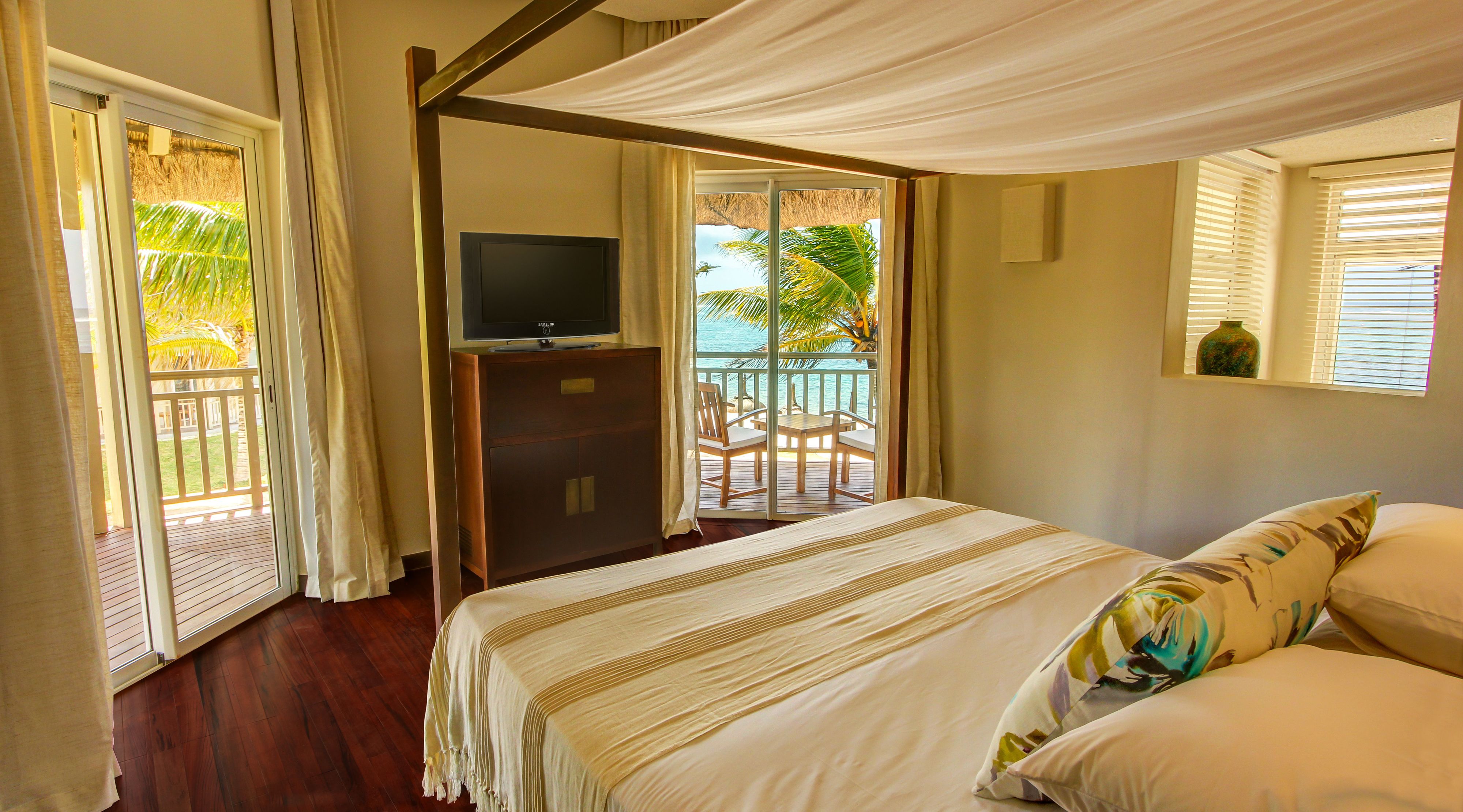 Un dormitorio con cama, televisor y balcón con vista al océano.
