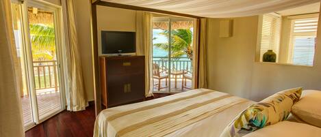 Un dormitorio con cama, televisor y balcón con vista al océano.