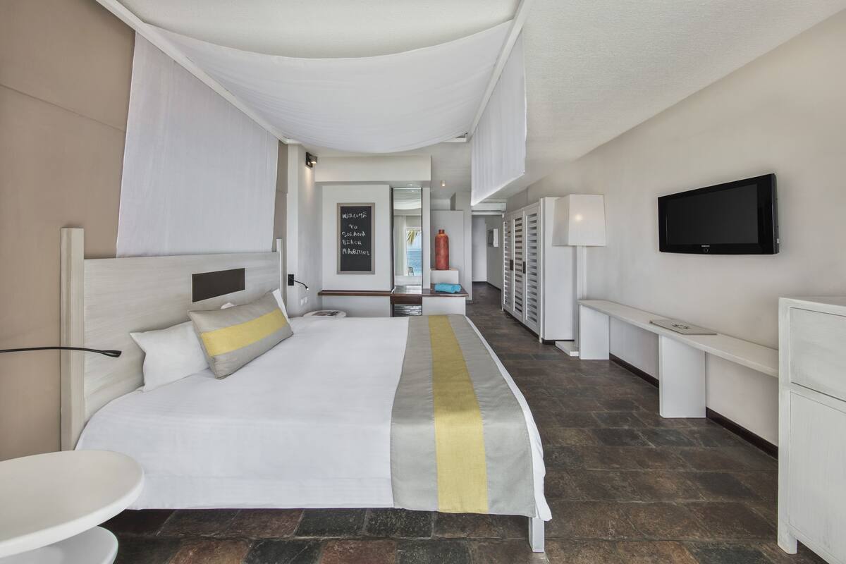 Une chambre d’hôtel avec un lit, des tables de chevet, une télévision, un bureau et une salle de bain que l’on aperçoit à l’arrière-plan.