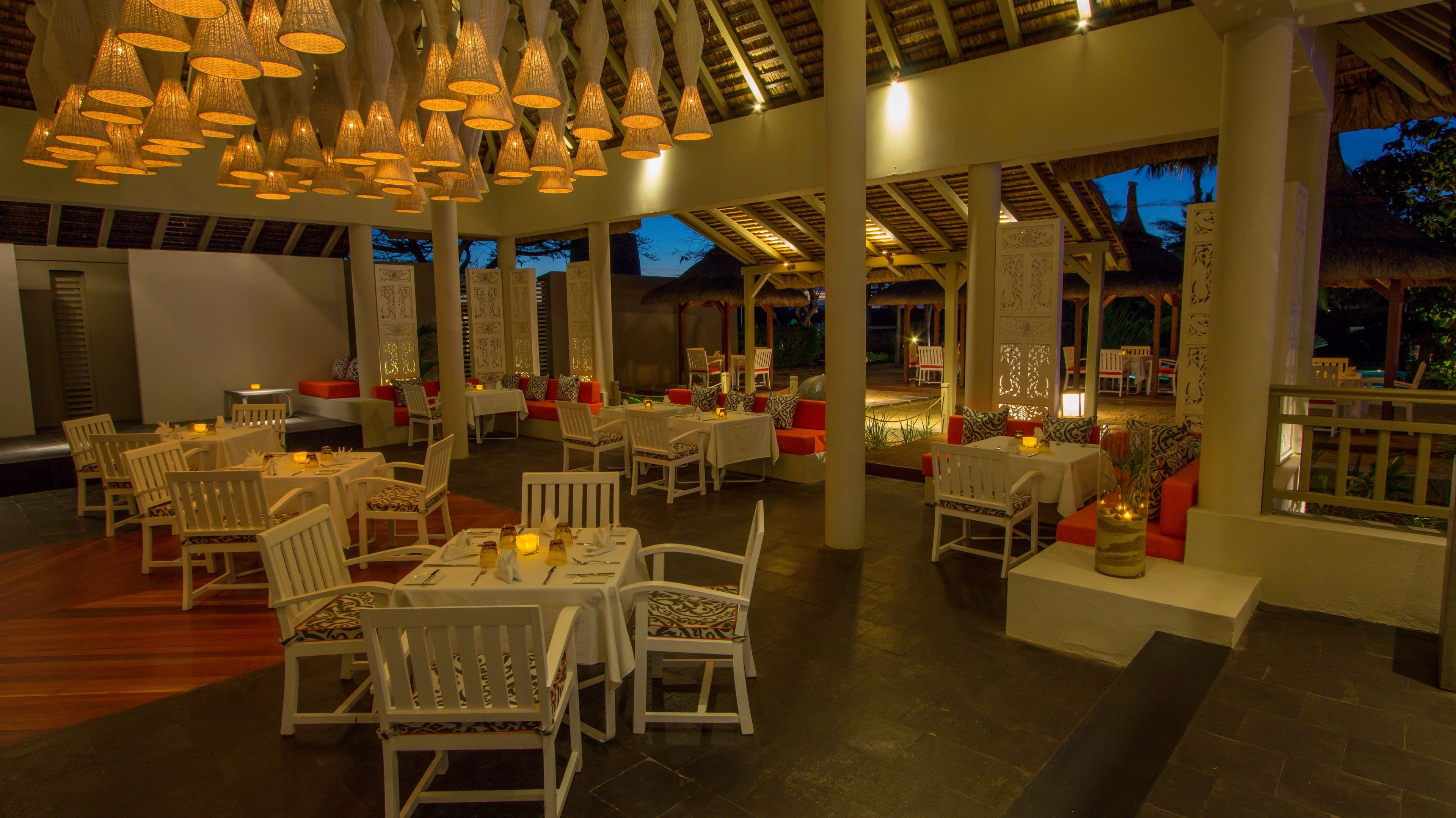 Un restaurant doté de nombreuses tables et chaises, d’un éclairage chaleureux et offrant une vue sur le ciel du soir.