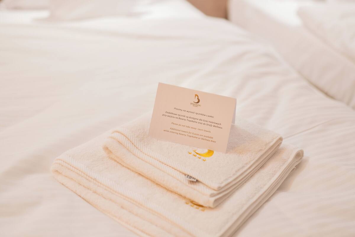 A neatly made bed with a folded towel and a card on top.