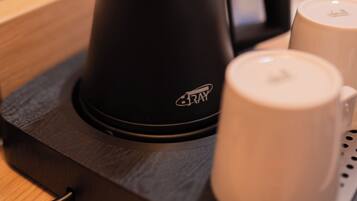 A black electric kettle with a handle and spout, a white mug, and a small bottle on a black tray.