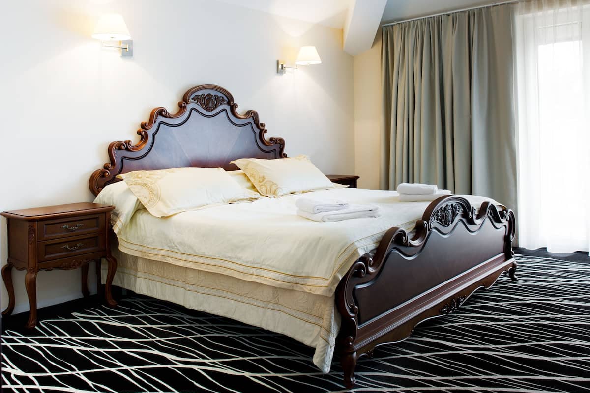 A neatly made bed with a dark wooden headboard, two bedside tables, and a patterned carpet.