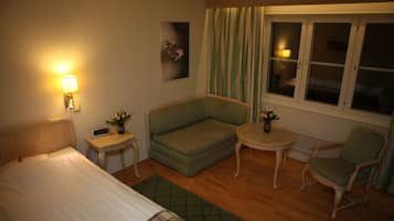 Ett hotellrum med en säng, en grön soffa, ett litet bord, en stol och ett fönster med gardiner.