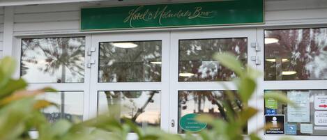 Entrada de un hotel con un letrero verde que dice "Hotel Montalvo Bro" y un cartel de bienvenida en un idioma extranjero.