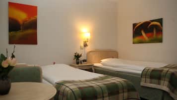 Une chambre d’hôtel avec deux lits, une table de chevet avec une lampe, une petite table ornée d’un vase de fleurs et deux tableaux accrochés aux murs.