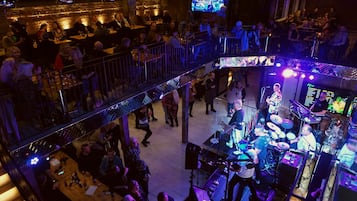 Un local con varios niveles, una tarima y equipo de DJ, rodeado de público sentado.