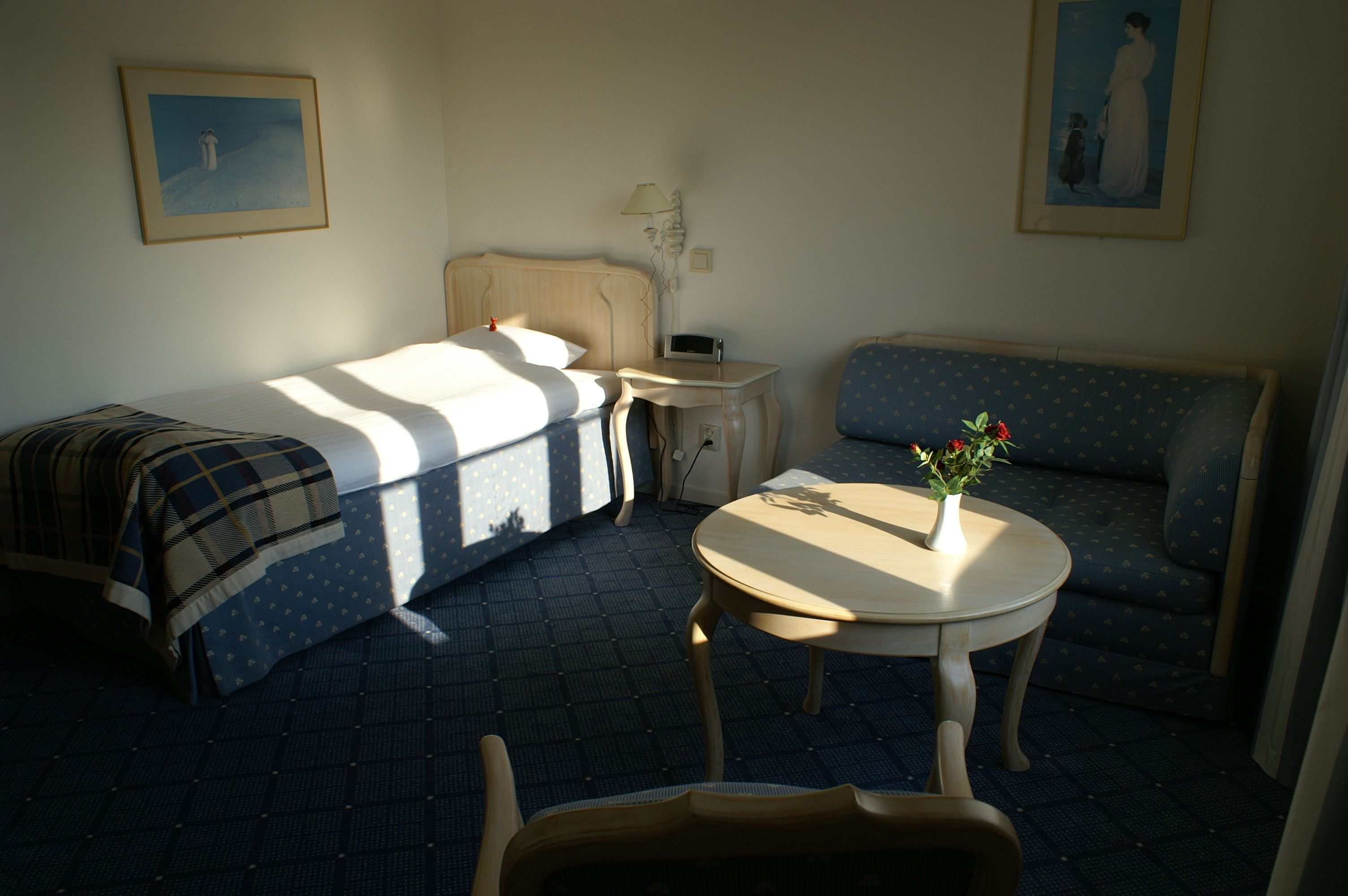 Een hotelkamer met een bed, een klein tafeltje met een vaas, een stoel, een bank en een nachtkastje.