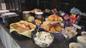 Un bufé con diferentes opciones de comida, incluyendo pasteles, pan y salsas.