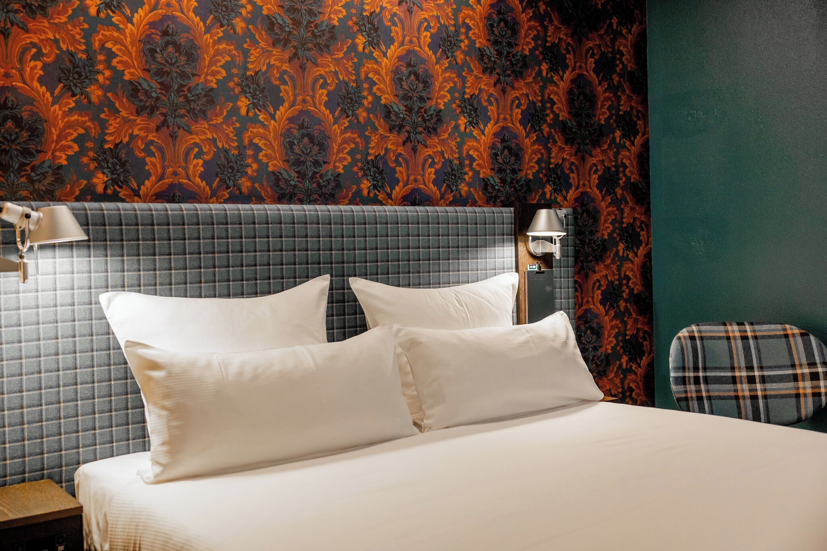 A neatly made bed with white linens and two pillows, a headboard with a checkered pattern, and a plaid-patterned chair.
