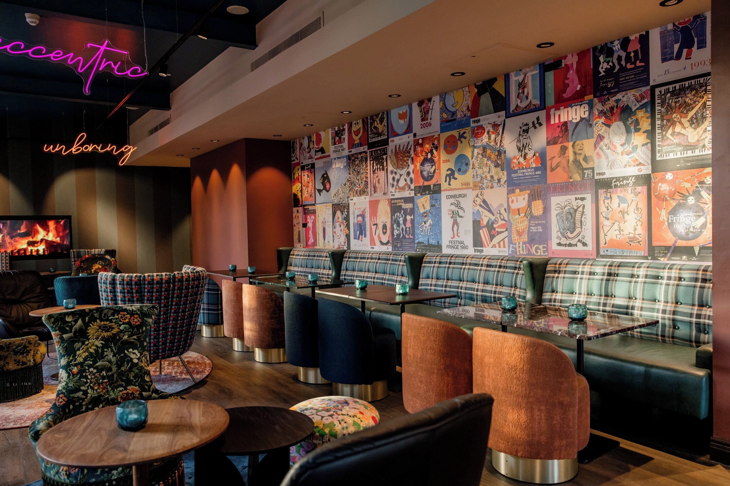 A cozy lounge area with plaid sofas, round tables, and a wall adorned with colorful posters.