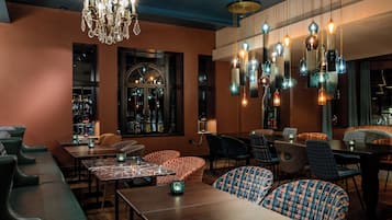 A restaurant with a bar area, seating with patterned cushions, and hanging pendant lights.