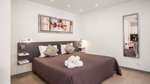 A modern hotel room with a large bed, a painting on the wall, a mirror, and a nightstand with a lamp. - Hôtel de L'Horloge (Paris)