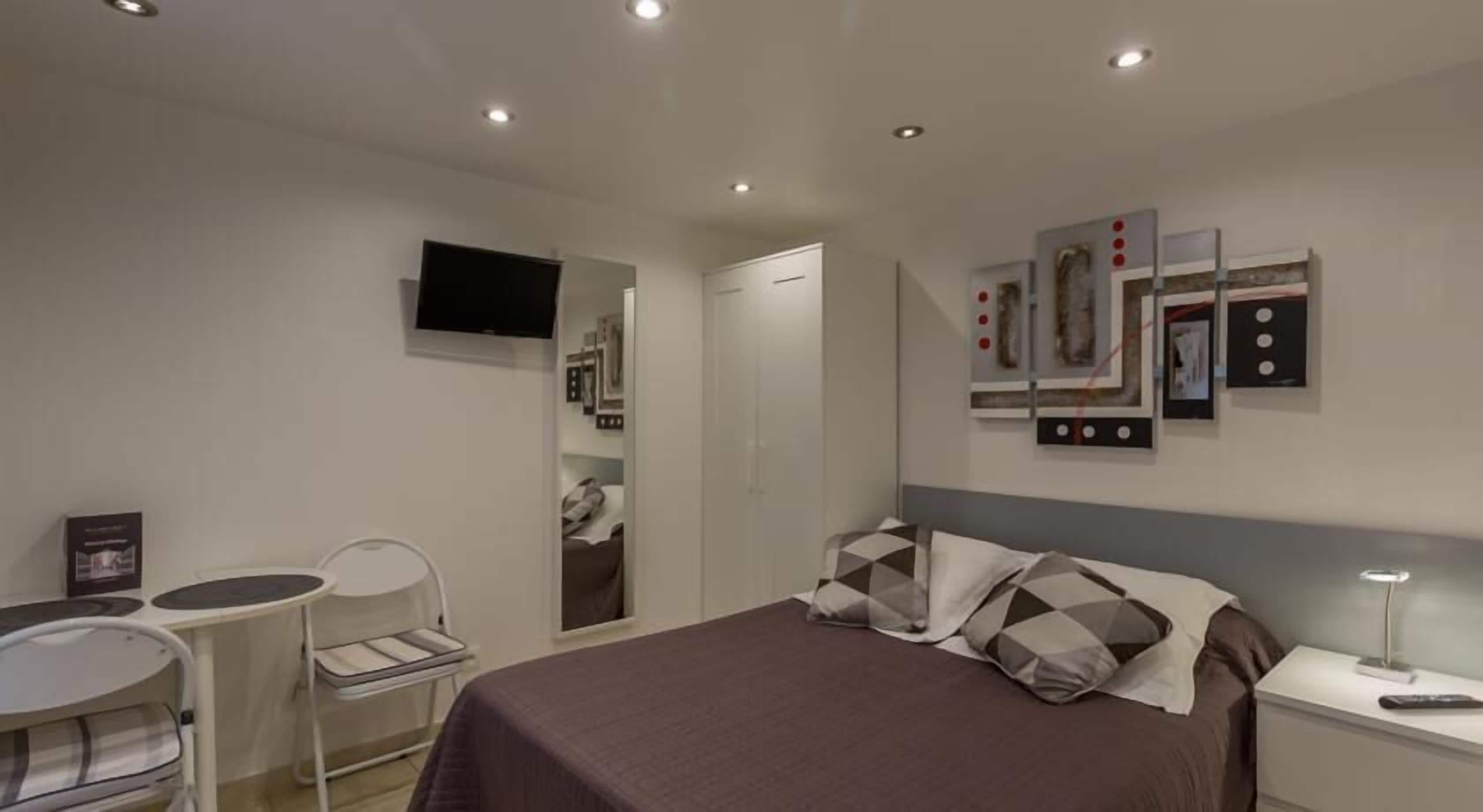 Habitación de hotel con cama, escritorio, silla, televisor y obras de arte en las paredes.