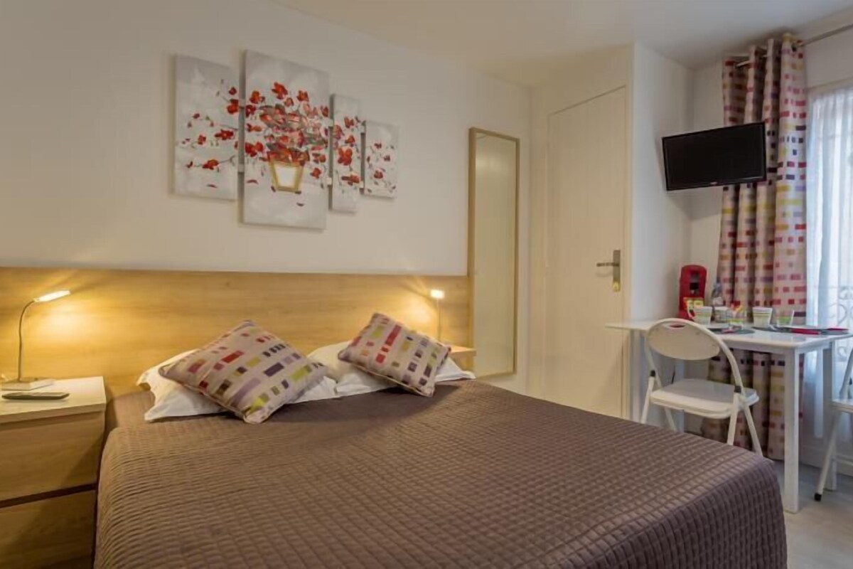 A hotel room with a bed, bedside lamps, a desk with a chair, a TV, and a window with curtains.