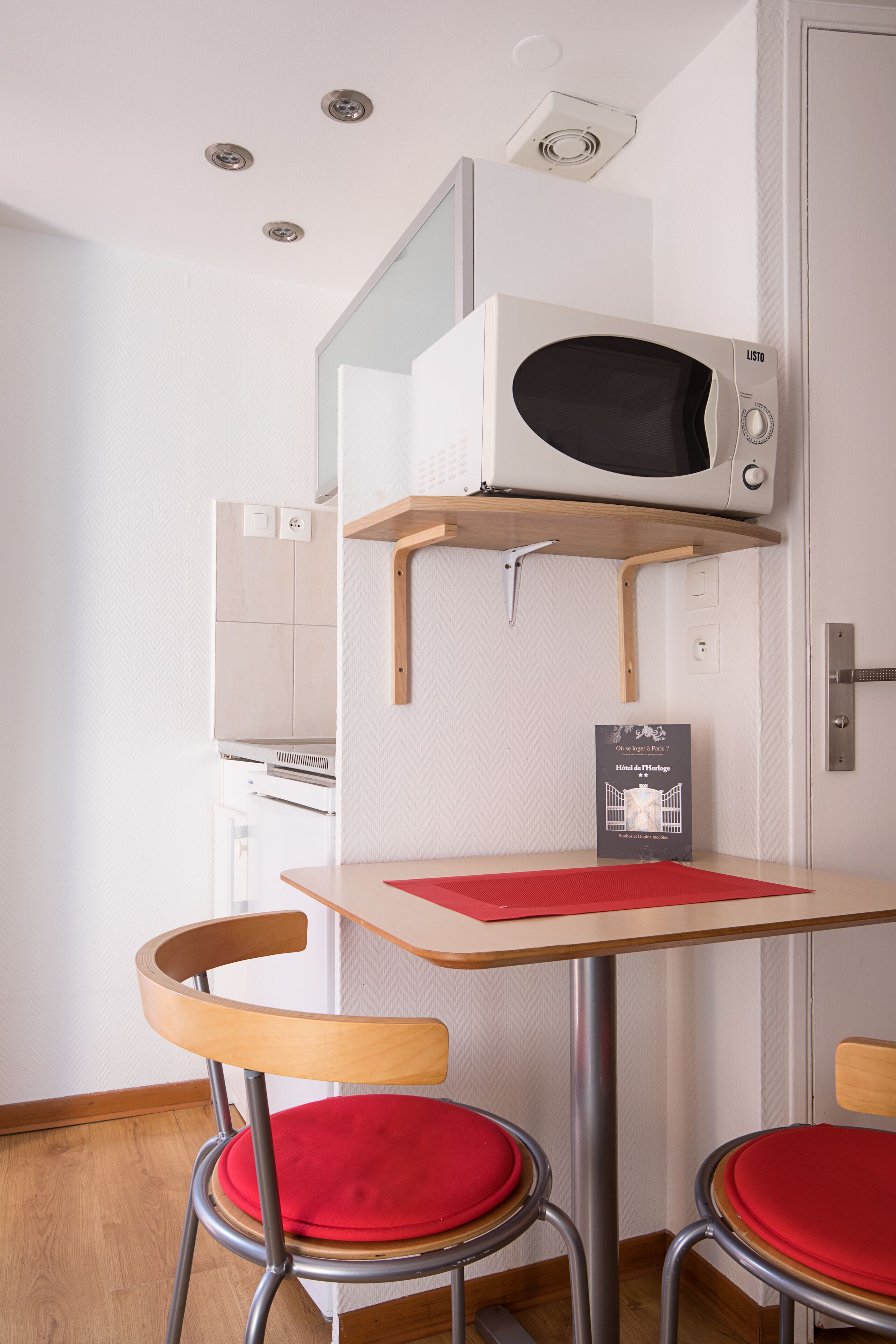 Une petite cuisine équipée comprenant un four à micro-ondes, une petite table et deux chaises avec des coussins rouges.