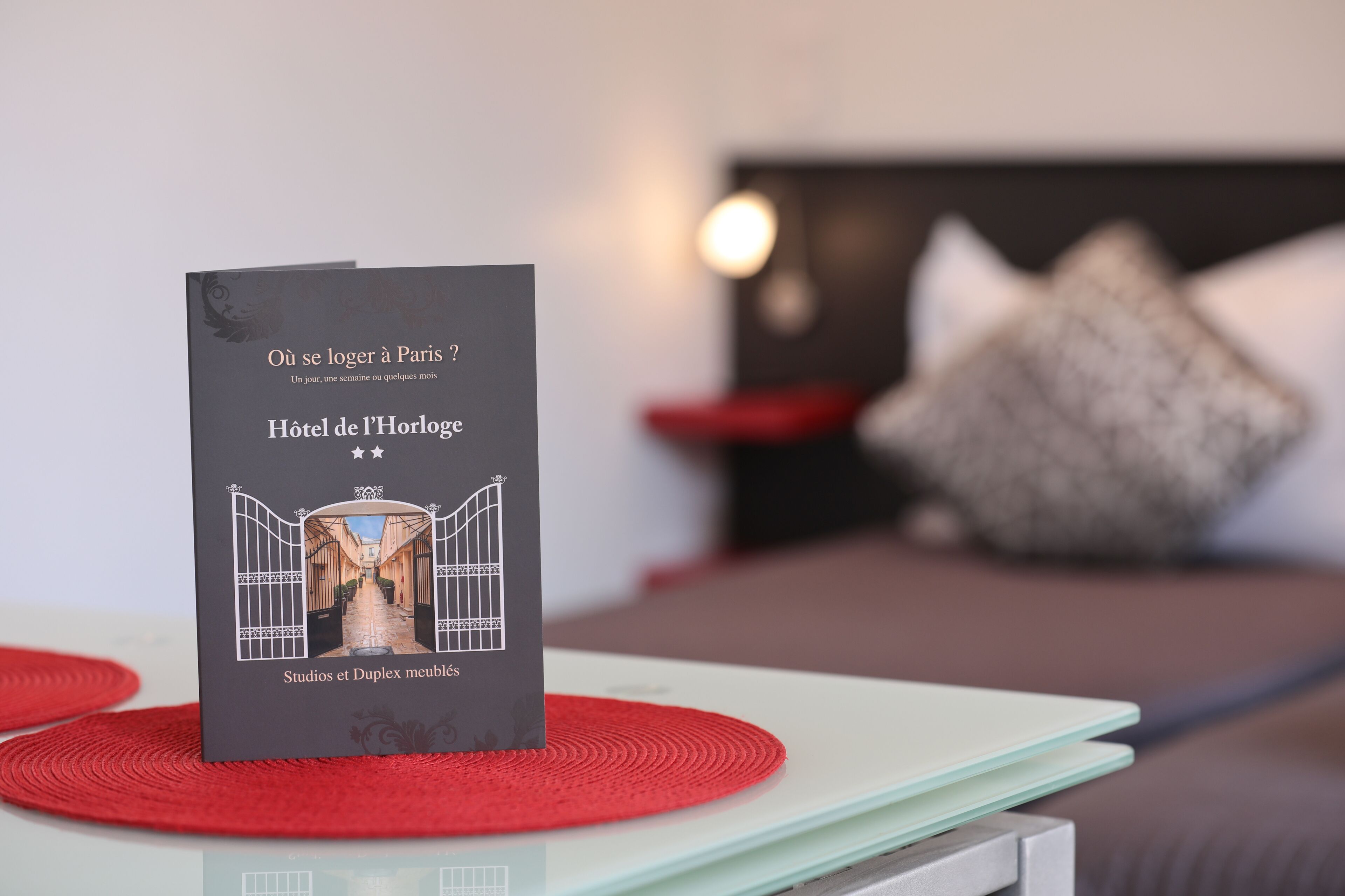 A hotel brochure titled "Hôtel de l'Horloge" with a view of the hotel's entrance and a bed with pillows in the background.