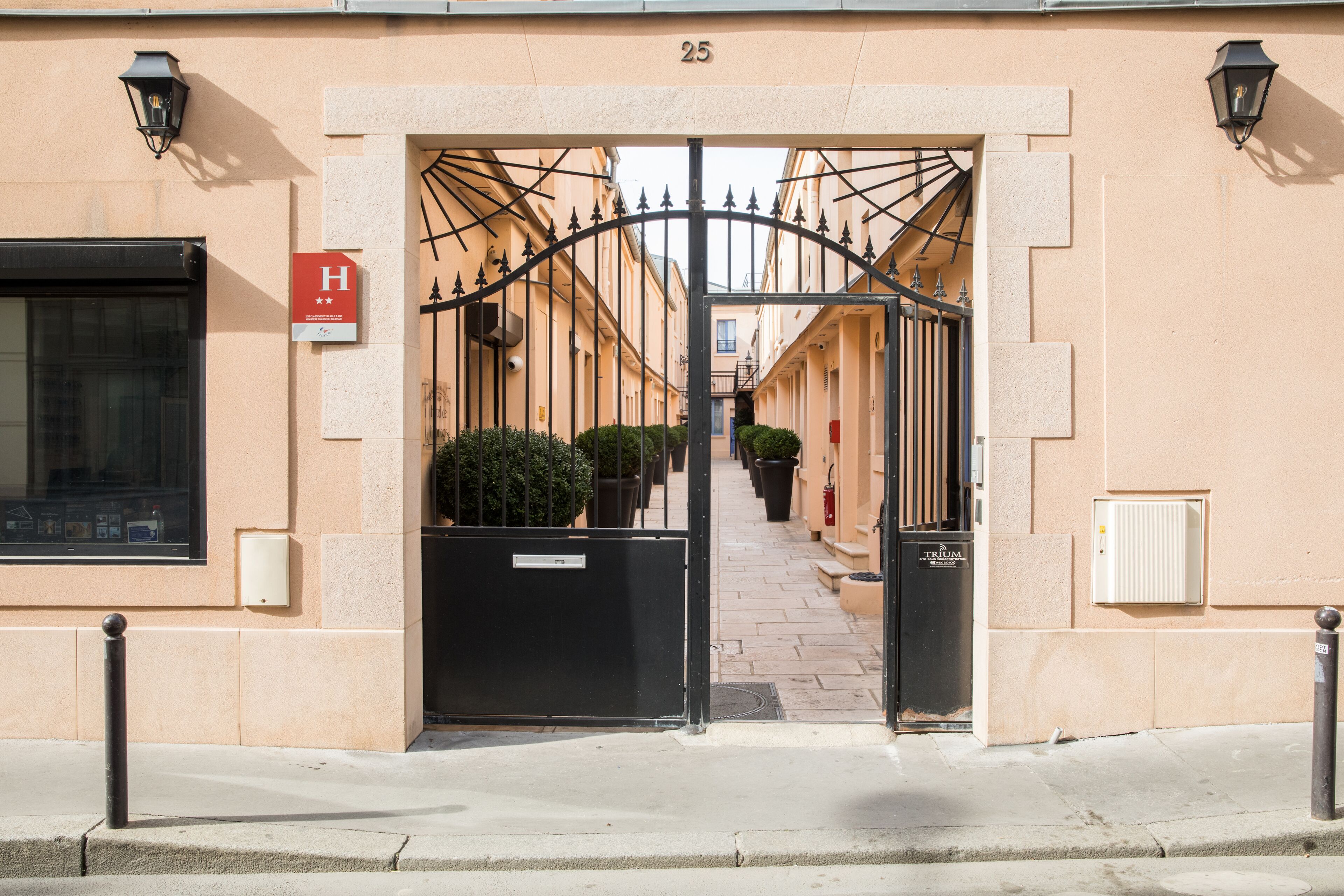 A hotel entrance with a wrought iron gate, a sign with an 'H', and a number '25' above the gate.