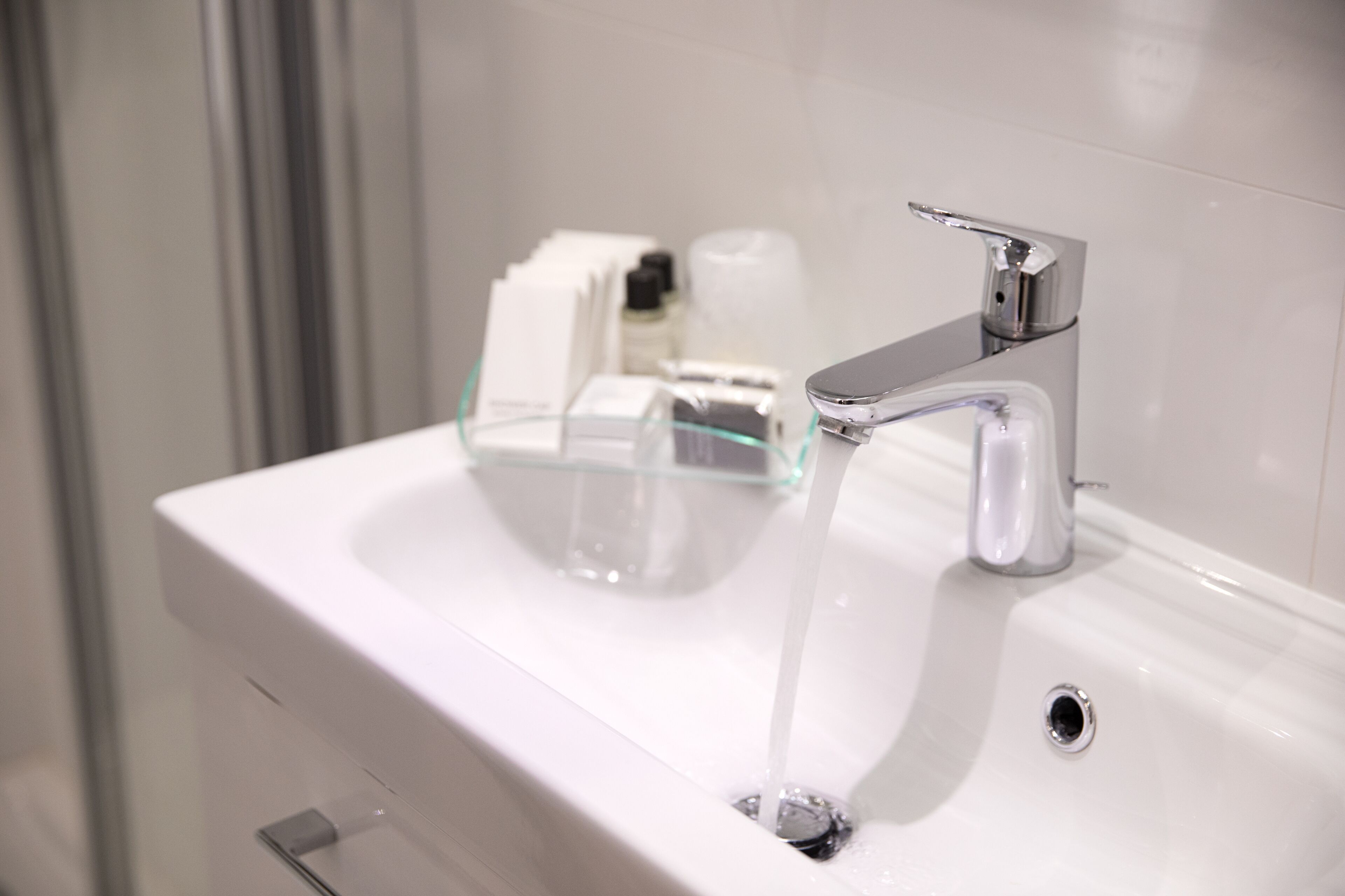 A modern bathroom with a white sink, chrome faucet, and glass soap dispenser.