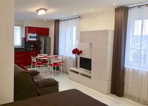 Un espace de vie compact comprenant un coin cuisine, un coin repas et un coin salon avec un téléviseur.