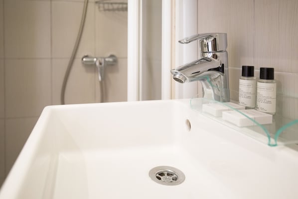 A white bathroom sink with chrome fixtures, a glass shelf holding toiletries, and a shower area in the background.