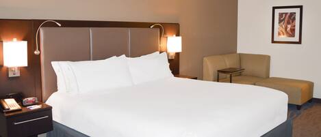 Habitación de hotel con una cama grande, lámparas de noche, una mesita, una silla y un cuadro en la pared.