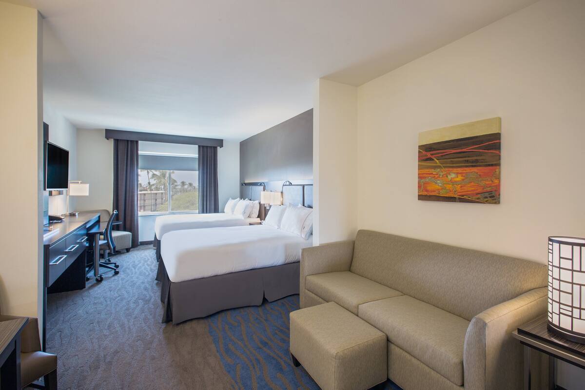 Una habitación de hotel con una cama, un sofá, un escritorio con una silla, un televisor y una ventana con cortinas.
