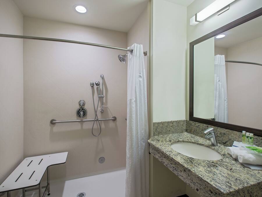 A bathroom with a shower, grab bar, and a sink with a mirror.