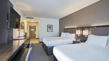A hotel room with two beds, a desk, a chair, a TV, and a bathroom.