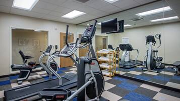Un gimnasio con cintas de correr, elípticas y un espejo grande.