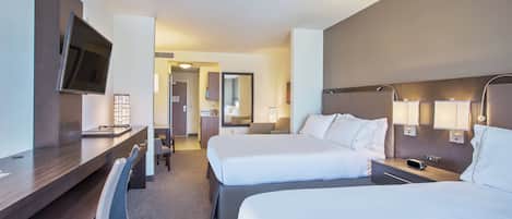 A hotel room with two beds, a desk, a chair, a TV, and a bathroom visible through an open door.