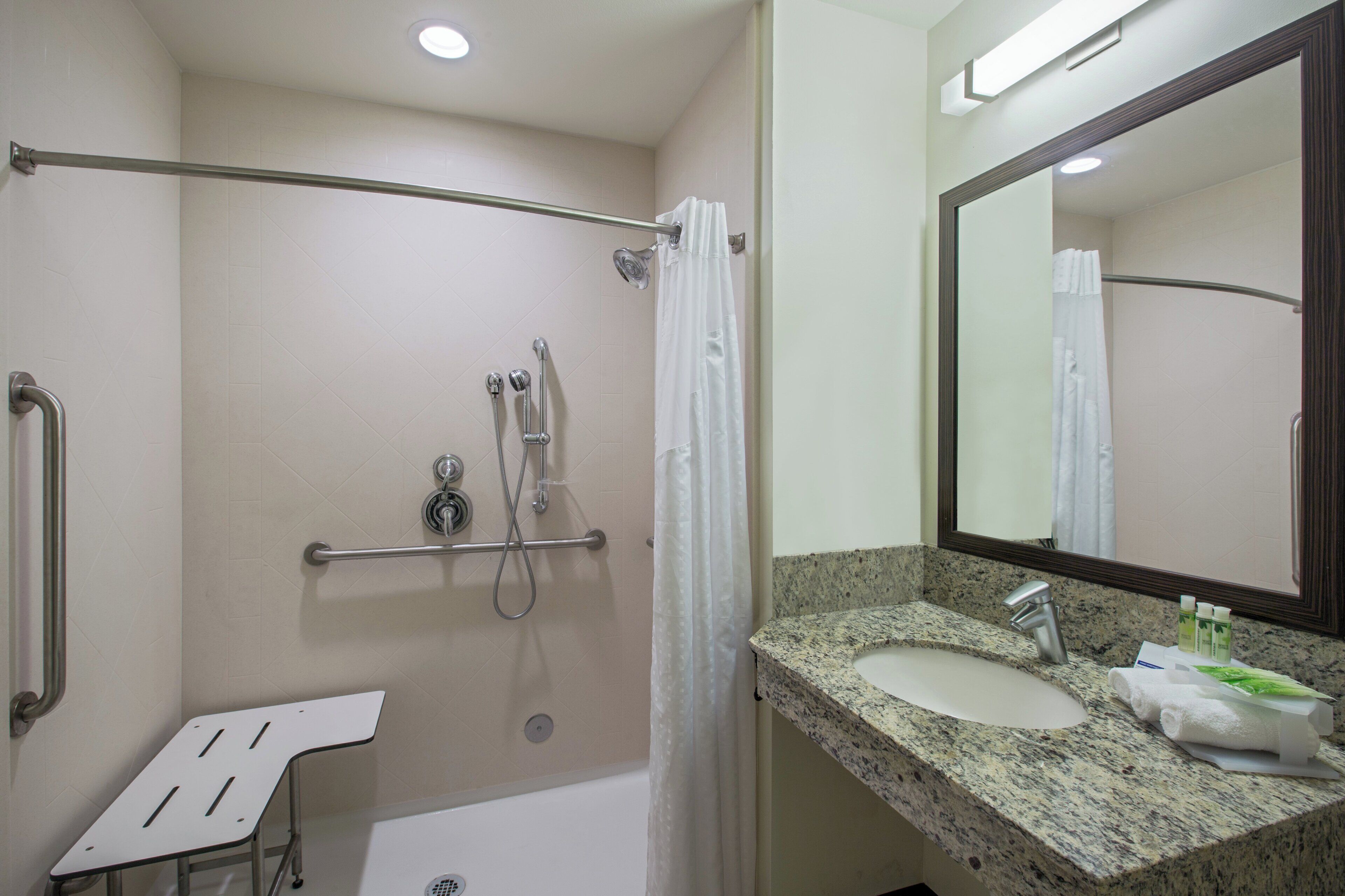 Baño con ducha, barra de apoyo, lavamanos y espejo.