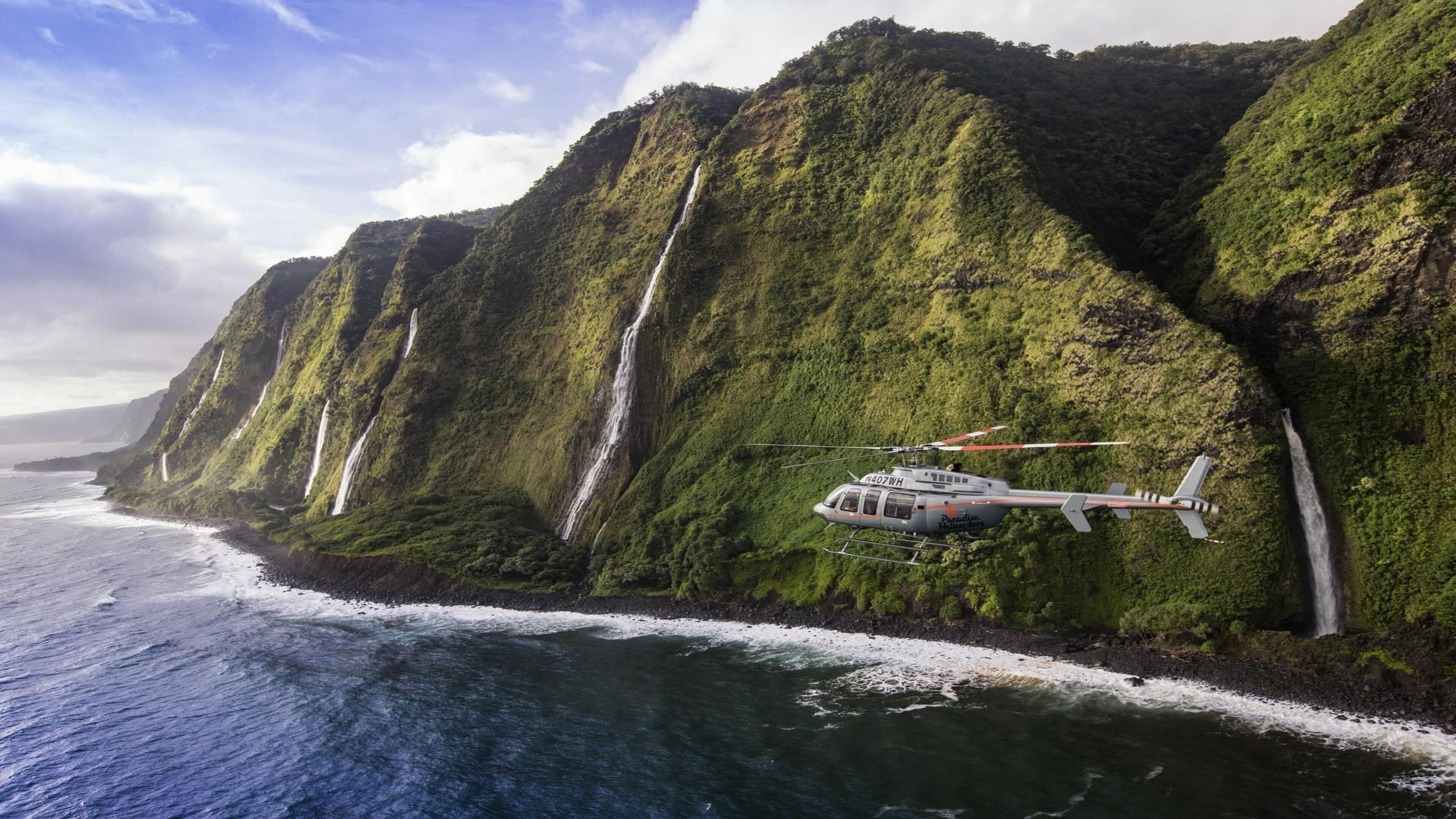 A helicopter flying over a coastal cliff with waterfalls.
