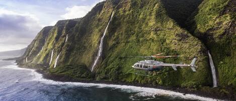 A helicopter flying over a coastal cliff with waterfalls.
