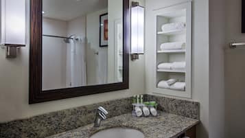A bathroom with a granite countertop, a white sink, a large mirror, a towel rack, and a shelf with neatly folded towels.