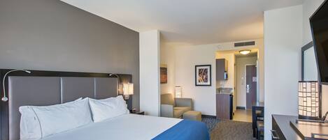 A hotel room with a large bed, a desk, a chair, and a small table.