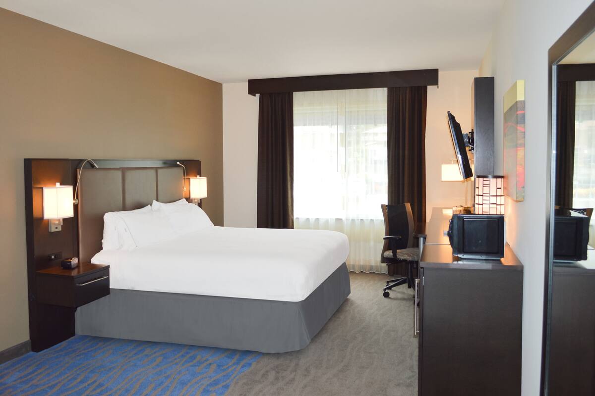 Una habitación de hotel con una cama grande, un escritorio con una computadora y un televisor.
