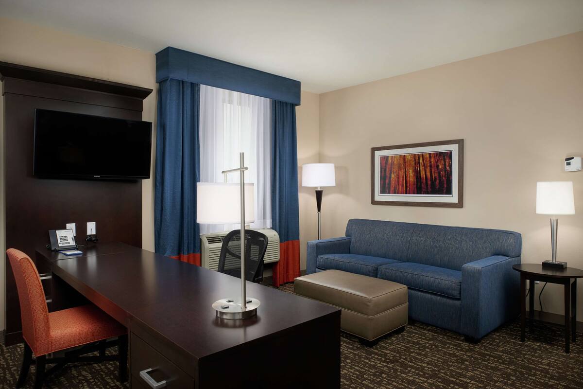 Ein Hotelzimmer mit Schreibtisch, Stuhl, Sofa und Hocker.