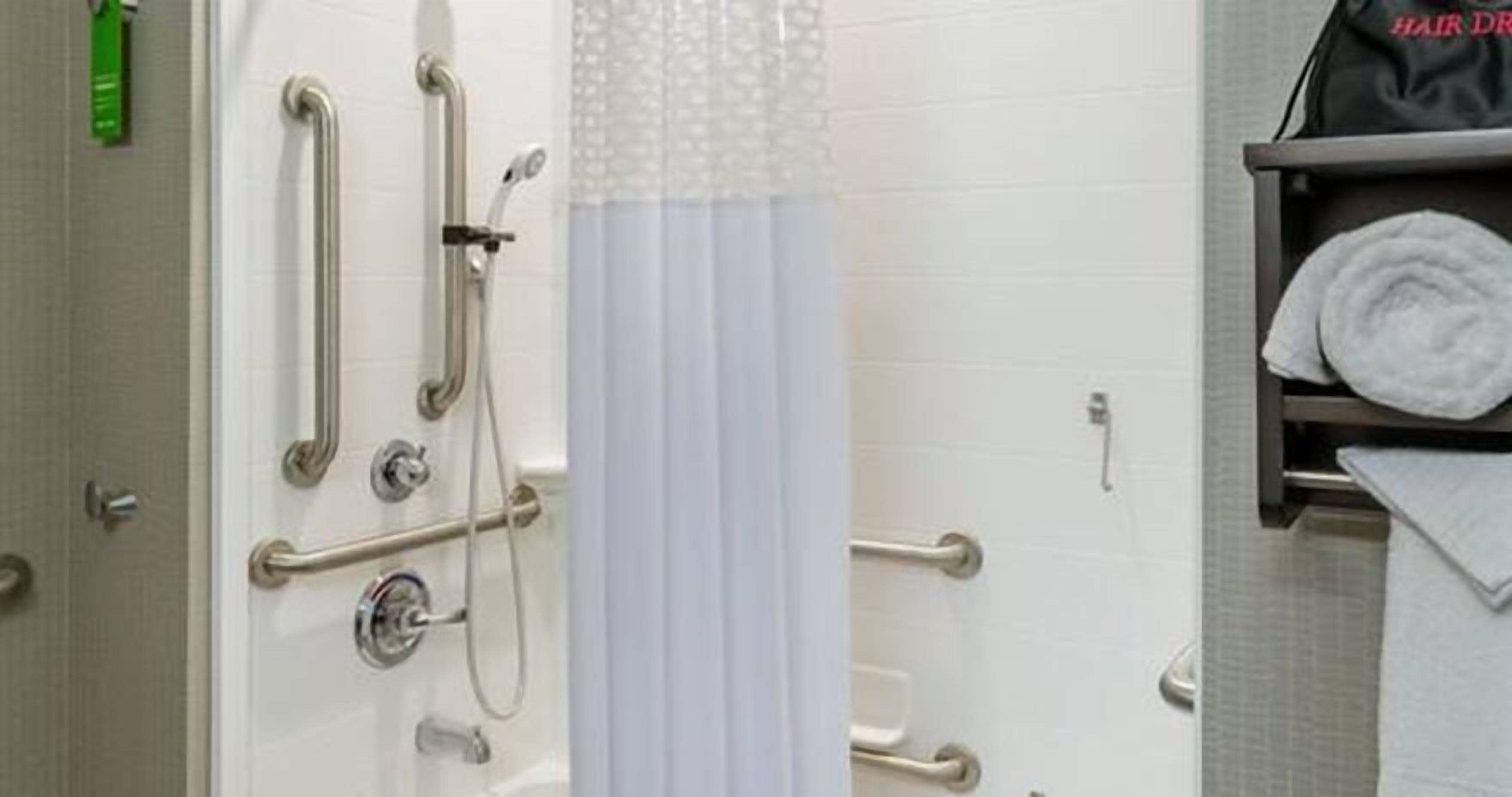A bathroom with a shower, grab bars, and a towel rack.