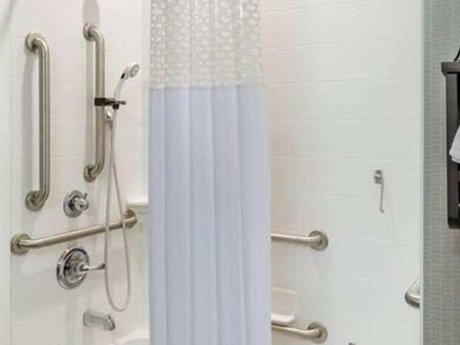 A bathroom with a shower, grab bars, and a towel rack.