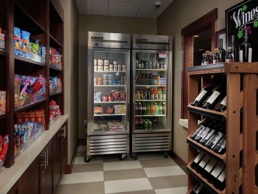Un pasillo de hotel con dos vitrinas refrigeradas llenas de aperitivos y bebidas, y una exhibición de vinos a la derecha.