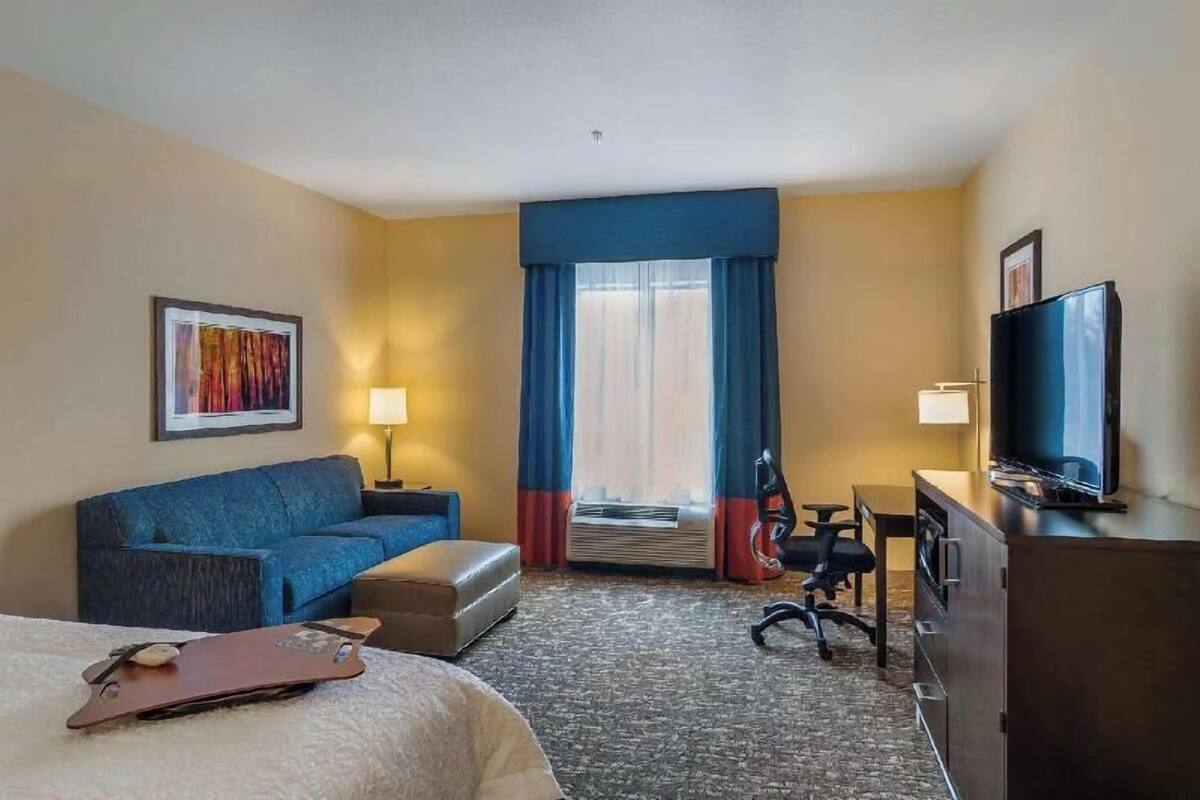 Ein Hotelzimmer mit Bett, Schreibtisch, Stuhl, Fernseher, einer Couch und einem Fenster mit Vorhängen.