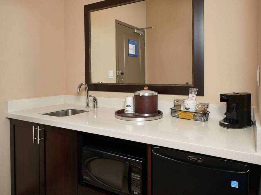 A hotel bathroom with a sink, mirror, coffee maker, and a microwave.
