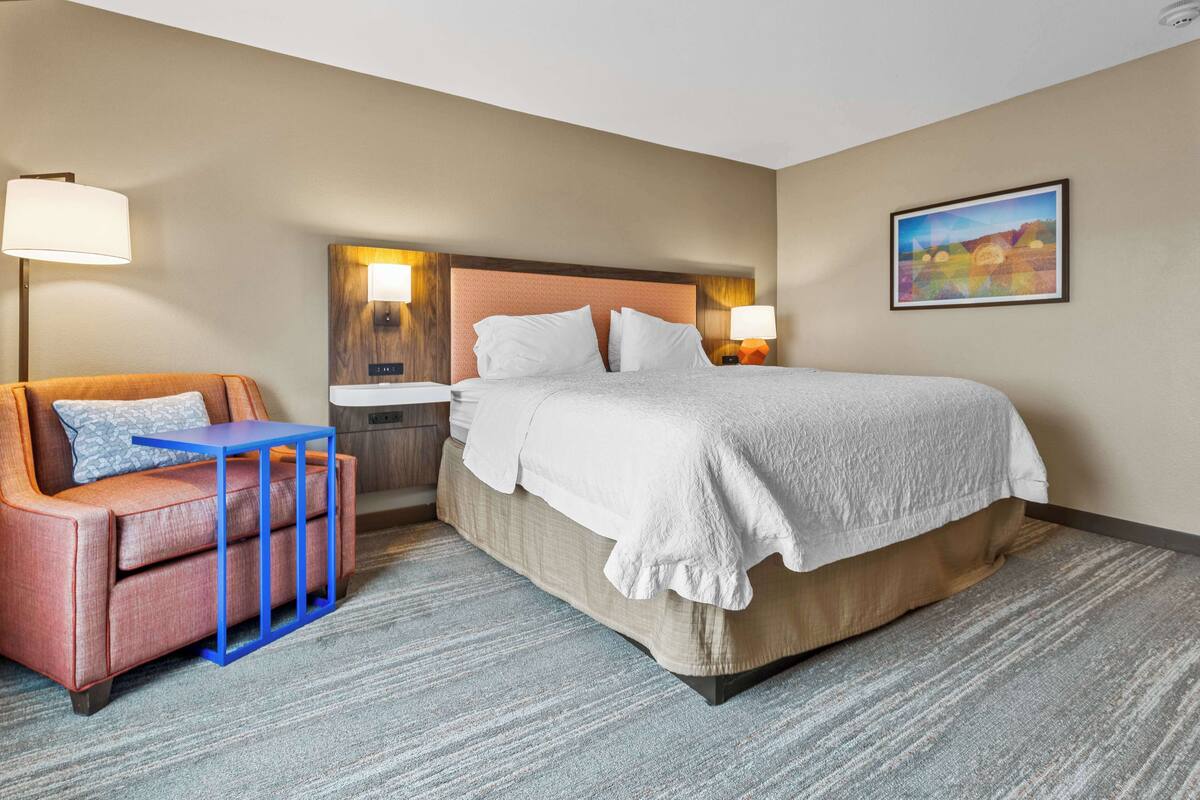 Quarto de hotel com cama, sofá, mesa pequena e um quadro na parede.