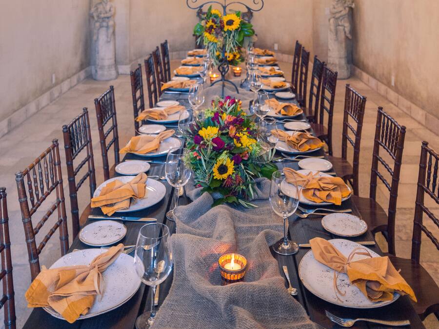 Uma longa mesa de jantar posta para uma refeição, com velas, flores e um candelabro.