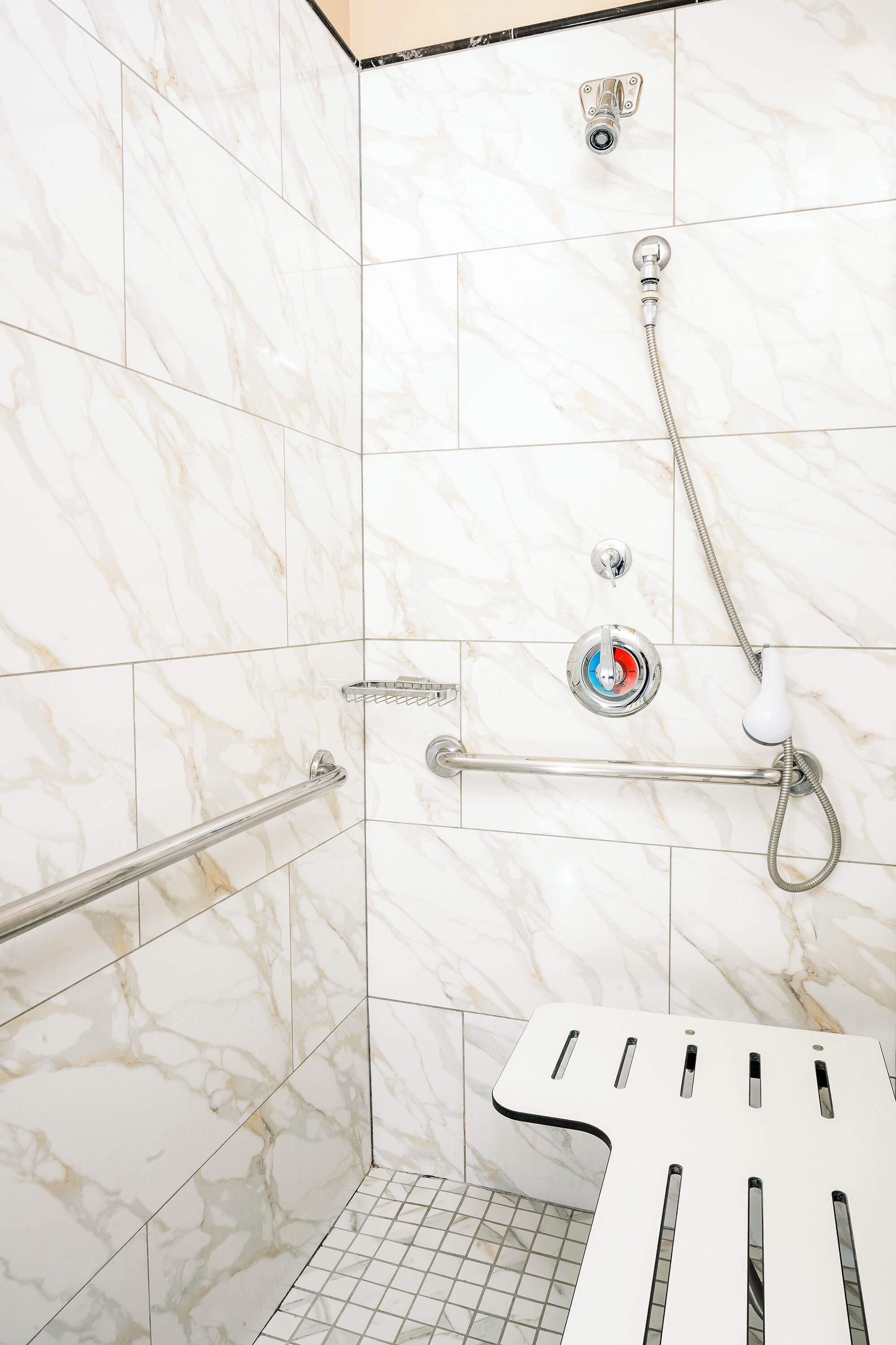 Zona de ducha con baranda, panel de control con un botón rojo y pared de azulejos blancos.